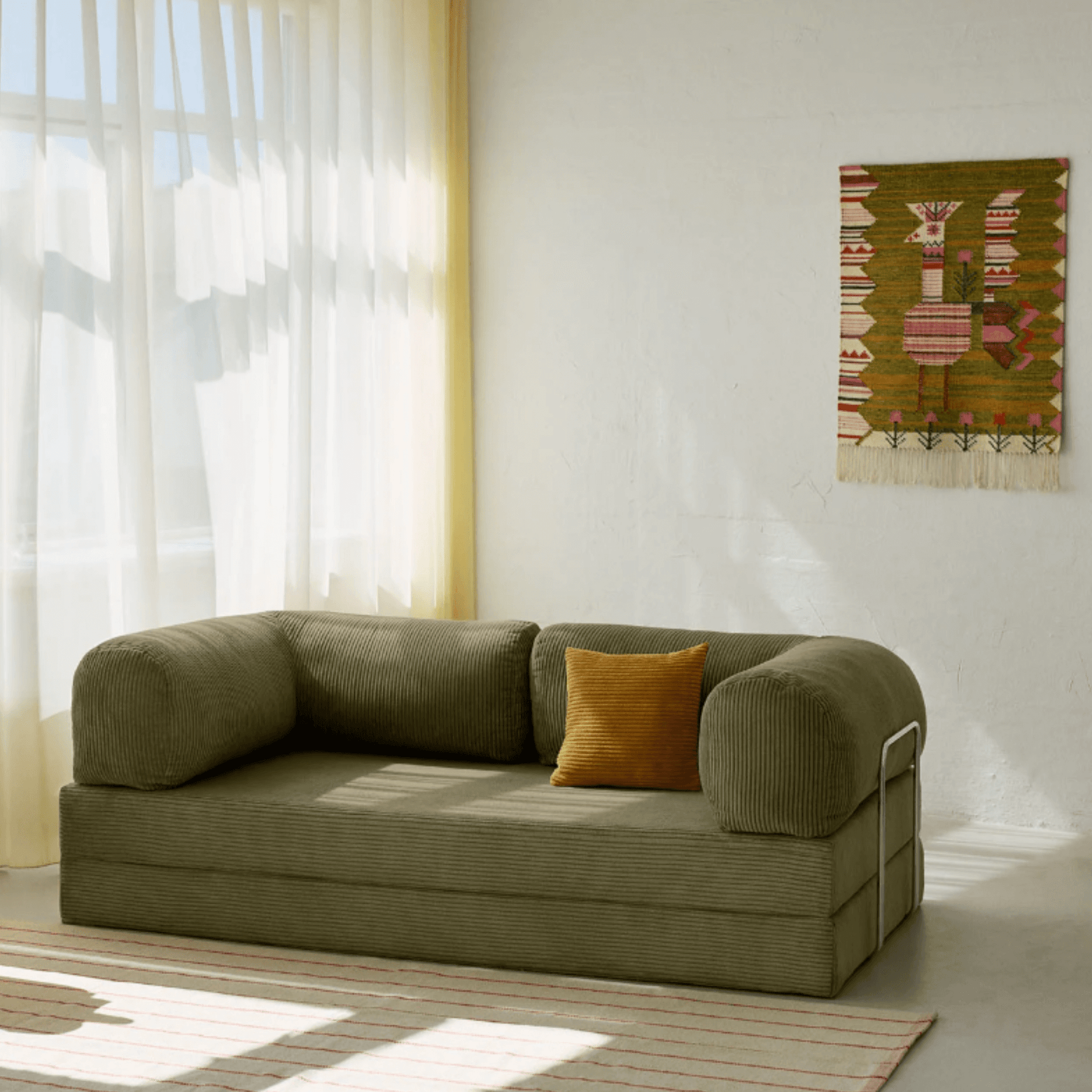 Primyhome Olive Green corduroy convertible sofa bed in a sunlit living room with minimalist decor and boho wall art