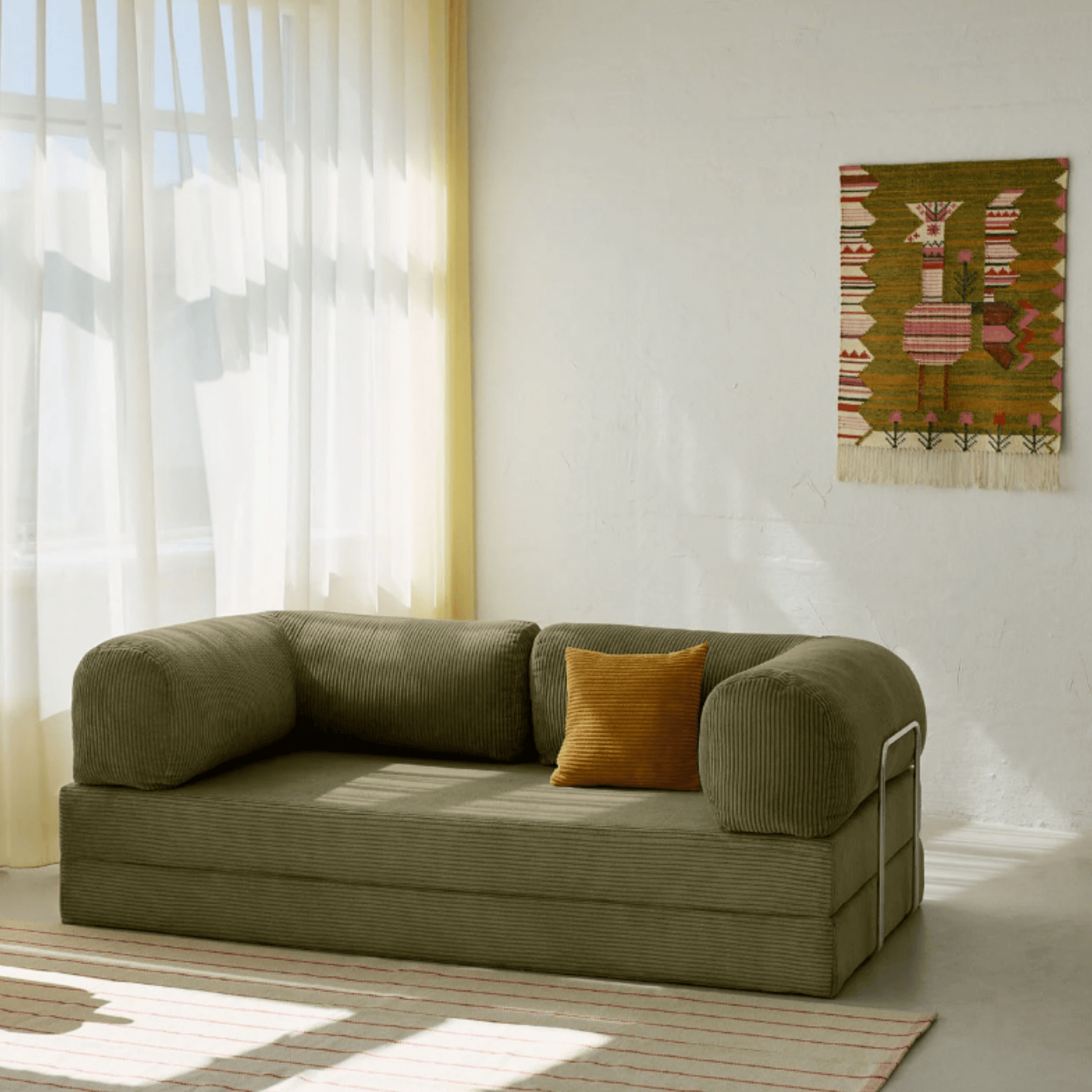 Primyhome Olive Green corduroy convertible sofa bed in a sunlit living room with minimalist decor and boho wall art